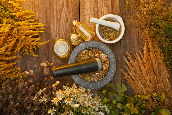 Top view of mortars and bottles near wildflowers and herbs on wooden surface — Stock Photo