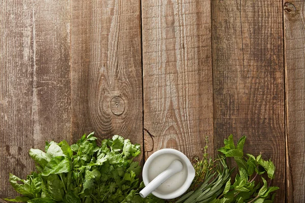 Vista dall'alto di malta bianca con pestello su superficie di legno con menta fresca, basilico, rosmarino, prezzemolo e timo — Foto stock