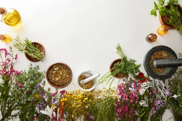 Draufsicht auf Mörser und Stößel mit Kräutermischungen in der Nähe von Blumen auf weißem Hintergrund — Stockfoto