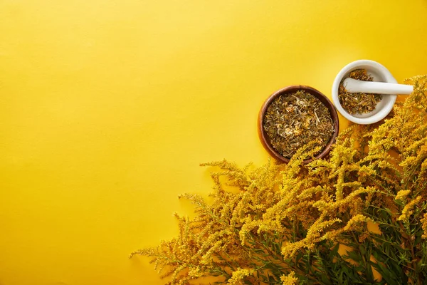 Vista dall'alto di malte con miscela di erbe vicino a mazzi di verghe d'oro su sfondo giallo — Foto stock