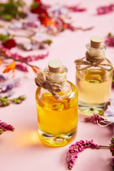 Vista de cerca de botellas con aceite cerca de flores silvestres frescas sobre fondo rosa - foto de stock