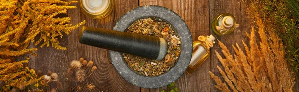 Panoramic shot of mortar and pestle dry herbal blend near bottles on wooden table — Stock Photo