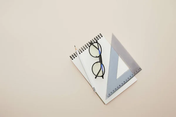 Top view of glasses, pencil and triangle ruler on notebook isolated on beige — Stock Photo