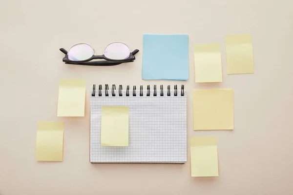 Top view of blank sticky notes on notebook near glasses isolated on beige — Stock Photo