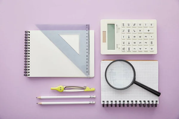 Vue de dessus de la loupe et du triangle de la règle sur les ordinateurs portables près de la calculatrice et de la papeterie isolées sur violet — Photo de stock