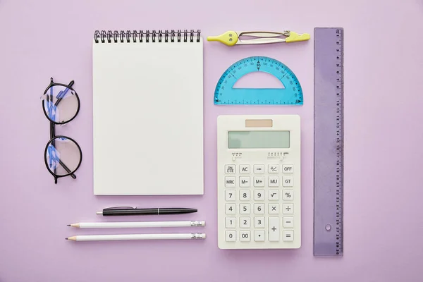 Vue du haut des règles et de la calculatrice près du bloc-notes et de la papeterie isolés sur violet — Photo de stock