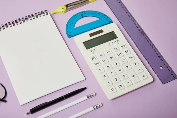 Rulers and calculator near notebook and pencils with pen isolated on purple — Stock Photo