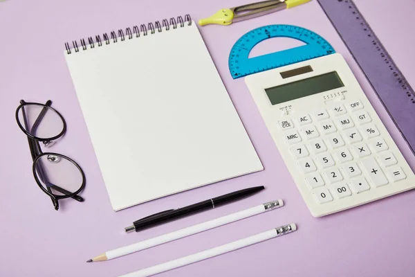 Lineale und Taschenrechner in der Nähe von Notizbuch und Brille isoliert auf lila — Stockfoto