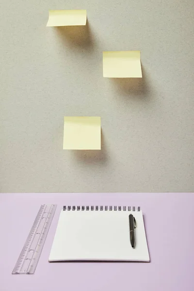 Cuaderno en blanco cerca de pluma, regla y notas adhesivas en gris y púrpura - foto de stock