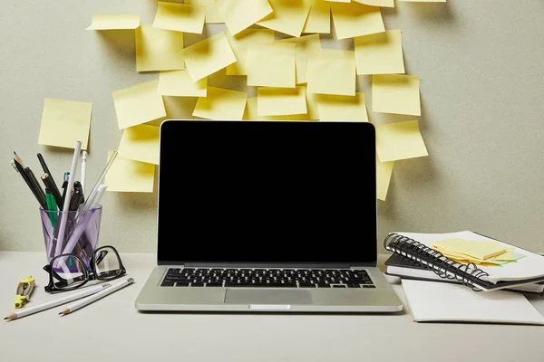 Laptop con pantalla en blanco cerca de notas adhesivas vacías y papelería en gris y blanco - foto de stock