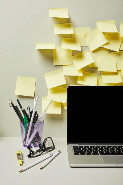 Computer portatile con schermo bianco vicino a note adesive vuote e portapenne con cancelleria su grigio e bianco — Foto stock