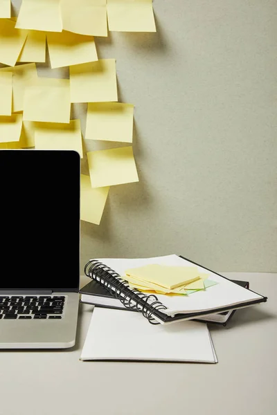 Ordinateur portable avec écran vierge près de notes collantes vides et des carnets sur gris et blanc — Photo de stock