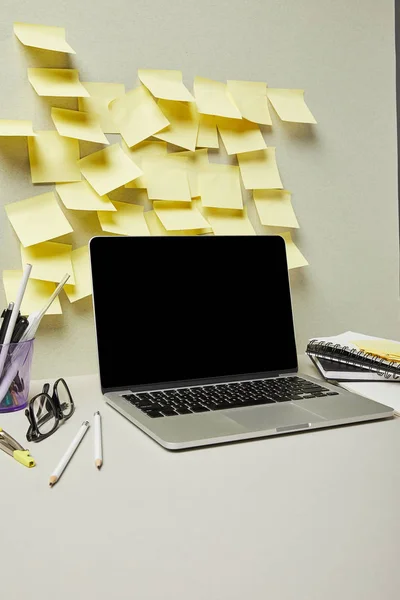 Laptop com tela em branco perto de notas pegajosas amarelas e artigos de papelaria em cinza e branco — Fotografia de Stock