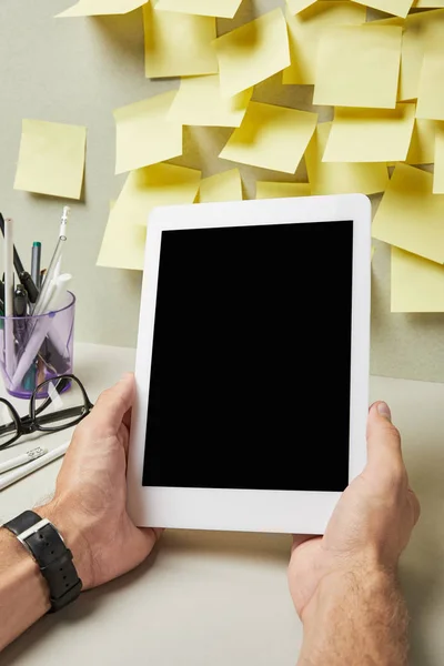 Vista cortada do homem segurando tablet digital com tela em branco perto de artigos de papelaria em cinza e branco — Fotografia de Stock
