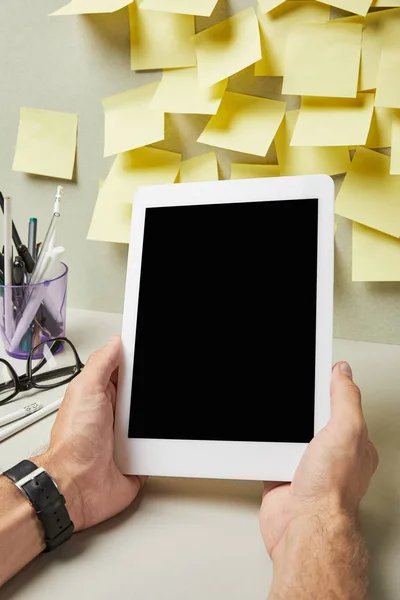 Vista recortada del hombre sosteniendo tableta digital con pantalla en blanco cerca de papelería en gris y blanco - foto de stock