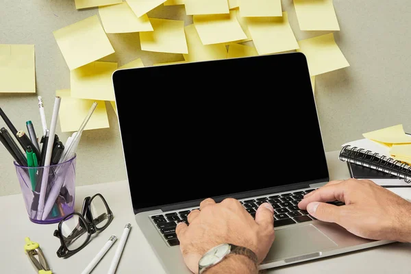 Ausgeschnittene Ansicht eines Mannes mit Laptop mit leerem Bildschirm in der Nähe von Schreibwaren und Notizbüchern auf grau-weiß — Stockfoto