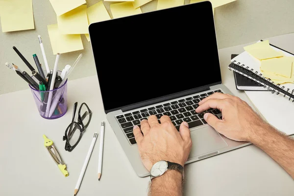 Vista recortada del hombre utilizando el ordenador portátil con pantalla en blanco cerca de papelería y notas adhesivas en gris y blanco - foto de stock