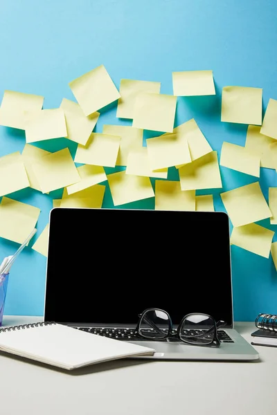 Laptop with blank screen near sticky notes, glasses and notebook on blue and white — Stock Photo