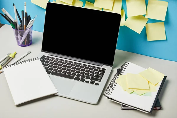 Laptop con pantalla en blanco cerca de notas adhesivas papelería y cuadernos en azul y blanco - foto de stock