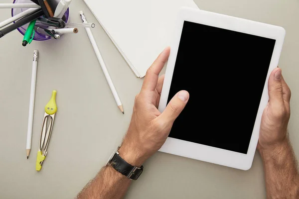 Vue du dessus d'un homme tenant une tablette numérique près d'un bloc-notes, de lunettes et d'articles de papeterie isolés sur gris — Photo de stock