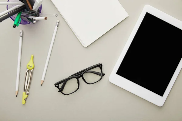 Vista superior de la tableta digital con pantalla en blanco cerca de papelería y gafas aisladas en gris - foto de stock