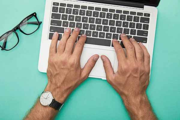 Top view of man typing on laptop near glasses isolated on turquoise — Stock Photo