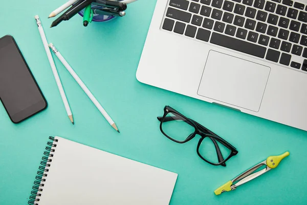 Top view of gadgets near glasses, stationery and notebook isolated on turquoise — Stock Photo