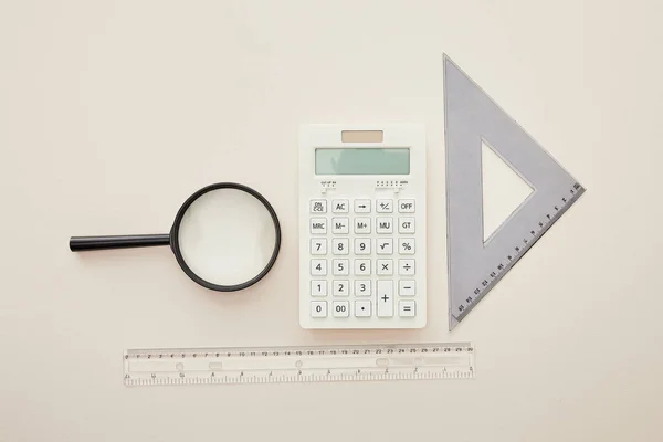 Top view of magnifier, rulers and calculator isolated on beige — Stock Photo