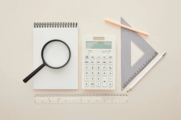 Top view of magnifier on notebook near stationery isolated on beige — Stock Photo