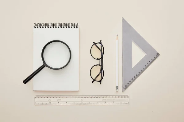 Top view of magnifier on notebook near glasses and rulers isolated on beige — Stock Photo