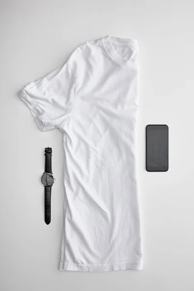 Flat lay com branco dobrado em meia t-shirt perto de relógios e smartphones em fundo branco — Fotografia de Stock