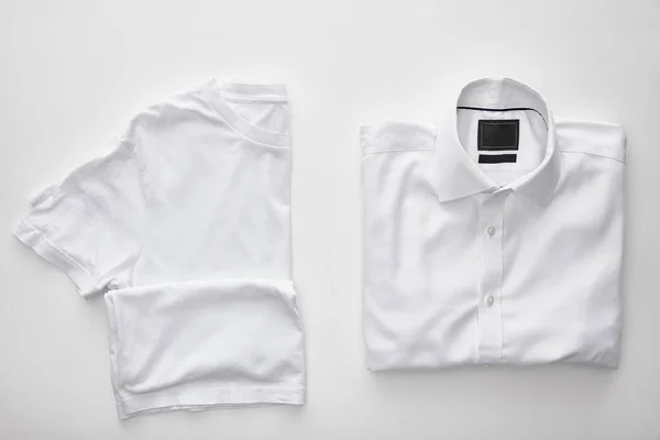 Вид сверху на пустую футболку рядом с клетчатой рубашкой на белом фоне — стоковое фото