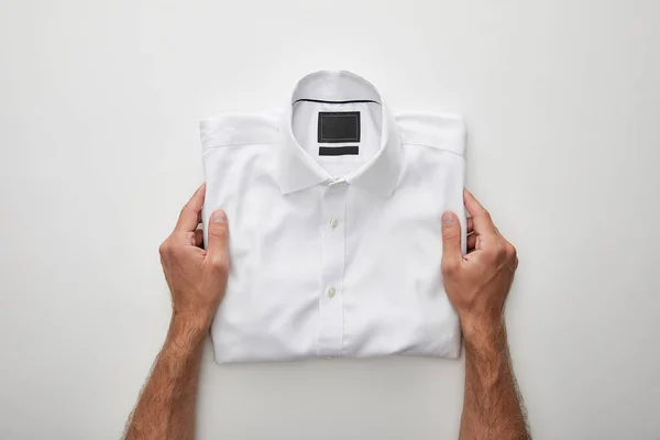 Vista cortada do homem segurando camisa dobrada no fundo branco — Fotografia de Stock