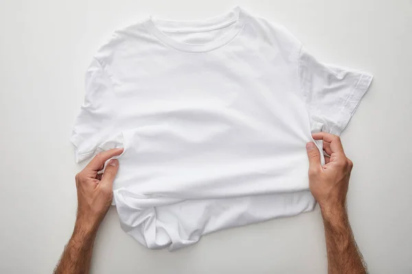 Vista ritagliata di uomo che tiene pianura t-shirt su sfondo bianco — Foto stock