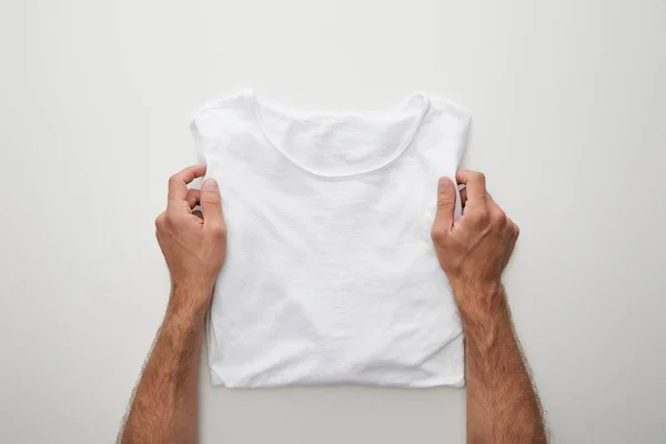 Vista ritagliata di uomo che tiene pianura piegato t-shirt su sfondo bianco — Foto stock