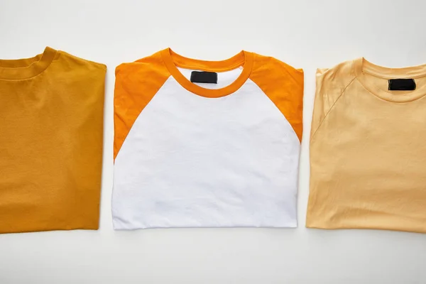 Top view of ochre, beige and orange folded t-shirts on white background — Stock Photo