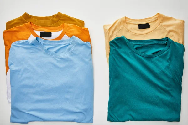 Vue du dessus des t-shirts beige, orange, bleu, turquoise et ocre sur fond blanc — Photo de stock