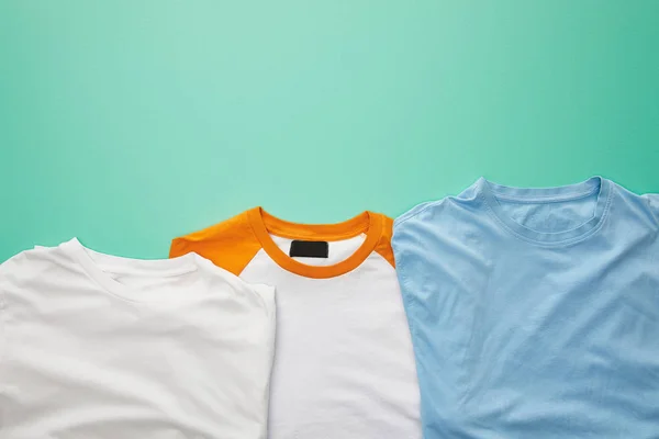 Top view of folded plaid color t-shirts on turquoise background — Stock Photo