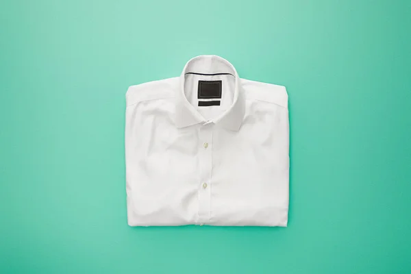 Draufsicht auf schlichtes weißes gefaltetes Hemd auf türkisfarbenem Hintergrund — Stockfoto