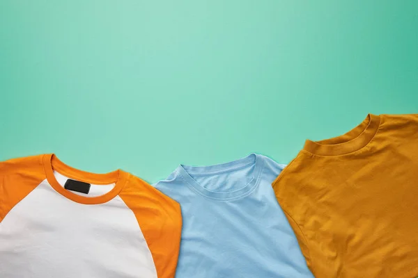 Vista superior de las camisetas plegadas de color naranja, azul y ocre sobre fondo turquesa - foto de stock