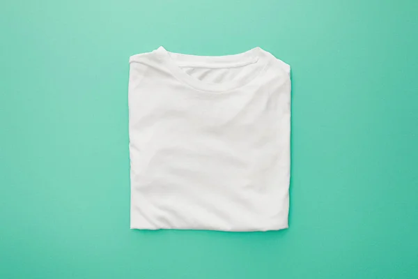 Vue du dessus du t-shirt blanc plié blanc sur fond turquoise — Photo de stock