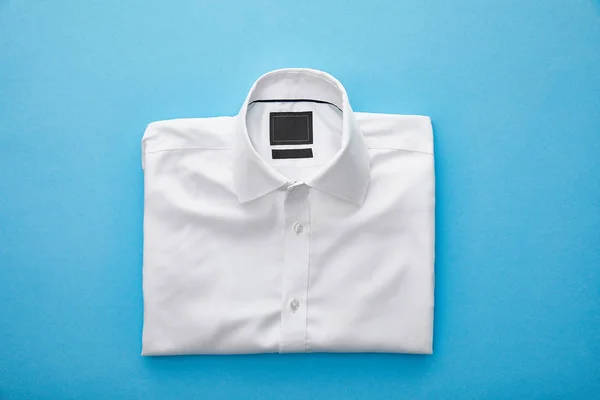 Top view of plain white folded shirt on blue background — Stock Photo