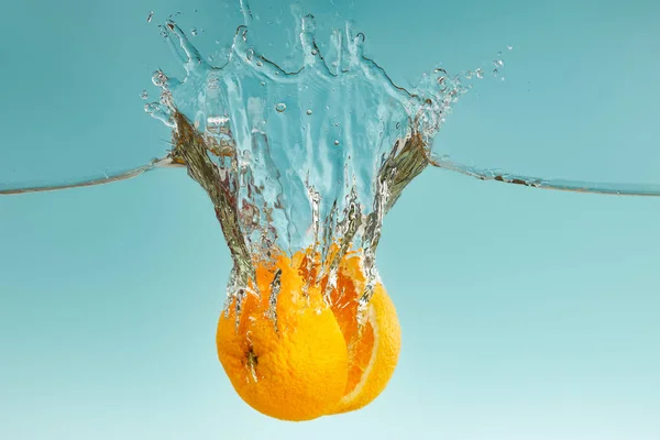 Ripe orange halves falling in water with splashes on blue background — Stock Photo