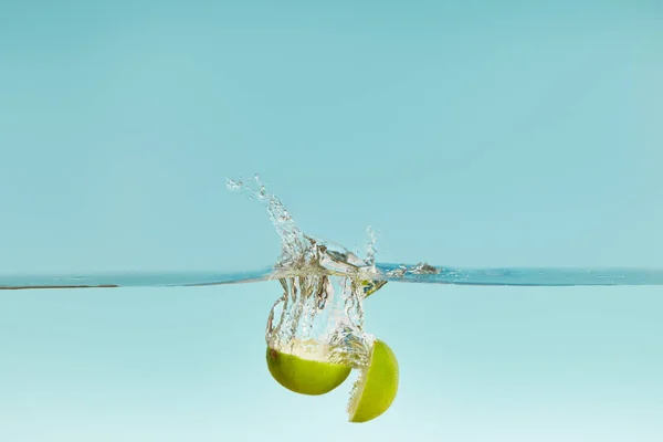 Ripe lime halves falling in water with splash on blue background — Stock Photo
