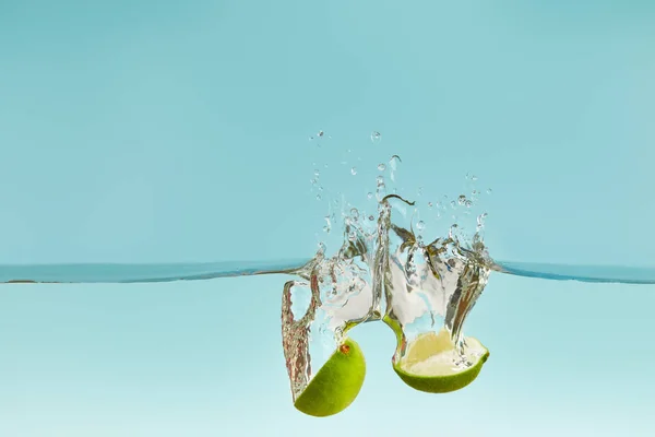 Metà di calce matura che cadono in acqua con spruzzi su fondo blu — Foto stock