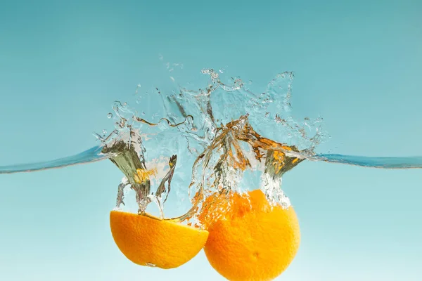 Naranja de corte maduro que cae en el agua con salpicaduras sobre fondo azul - foto de stock