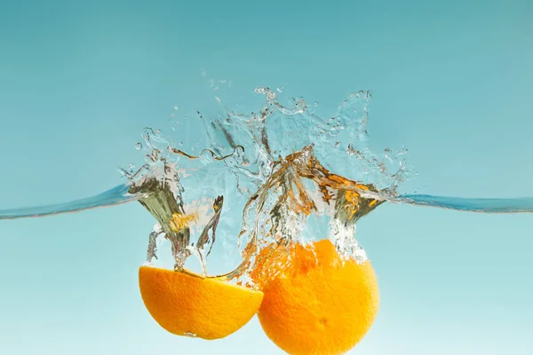 Laranja corte maduro caindo na água com salpicos no fundo azul — Fotografia de Stock