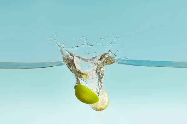 Metà mature di calce che cadono in profondità in acqua con spruzzi su sfondo blu — Foto stock