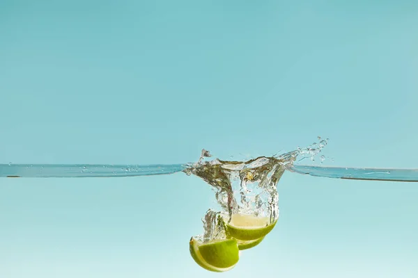 Kalkhälften fallen tief ins Wasser mit Spritzer auf blauem Hintergrund — Stockfoto