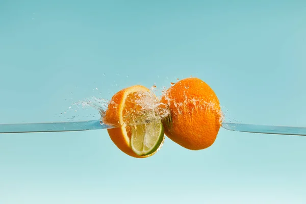 Mitades naranjas maduras cayendo en el agua con gotas sobre fondo azul - foto de stock